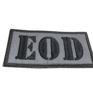 K&ouml;nnte beinhalten: Ein grauer gestickter Aufn&auml;her mit dem Wort "EOD" in schwarzen Buchstaben.