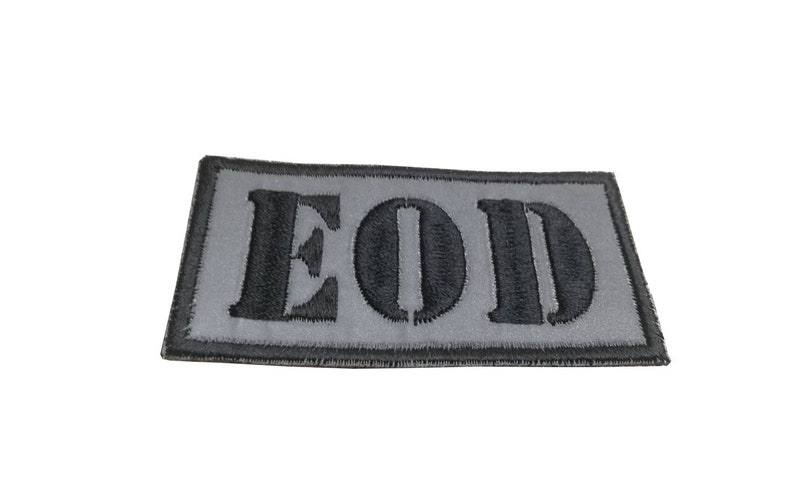 K&ouml;nnte beinhalten: Ein grauer gestickter Aufn&auml;her mit dem Wort "EOD" in schwarzen Buchstaben.