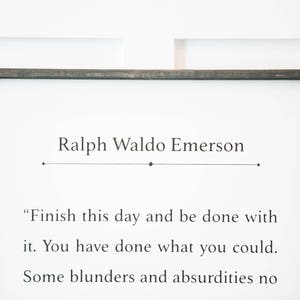 May include: A black framed sign with a white background and a quote by Ralph Waldo Emerson: "Finish this day and be done with it. You have done what you could. Some blunders and absurdities no"