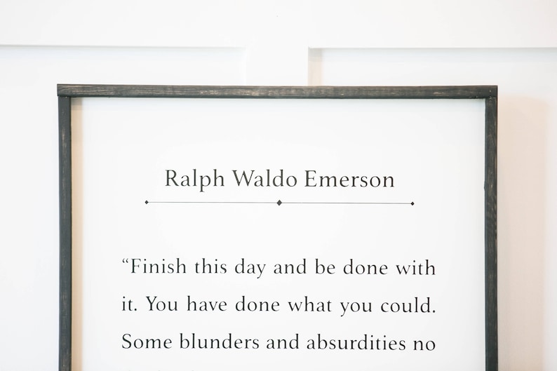 May include: A black framed sign with a white background and a quote by Ralph Waldo Emerson: "Finish this day and be done with it. You have done what you could. Some blunders and absurdities no"