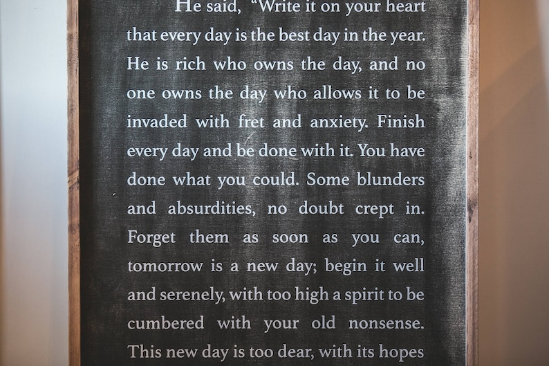 May include: Black chalkboard sign with white text that reads: "He said, 'Write it on your heart that every day is the best day in the year. He is rich who owns the day, and no one owns the day who allows it to be invaded with fret and anxiety. Finish every day and be done with it. You have done what you could. Some blunders and absurdities, no doubt crept in. Forget them as soon as you can, tomorrow is a new day; begin it well and serenely, with too high a spirit to be cumbered with your old nonsense. This new day is too dear, with its hopes"