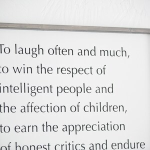 May include: A framed white sign with black text that reads "To laugh often and much, to win the respect of intelligent people and the affection of children, to earn the appreciation of honest critics and endure..." The frame is a muted gray color.