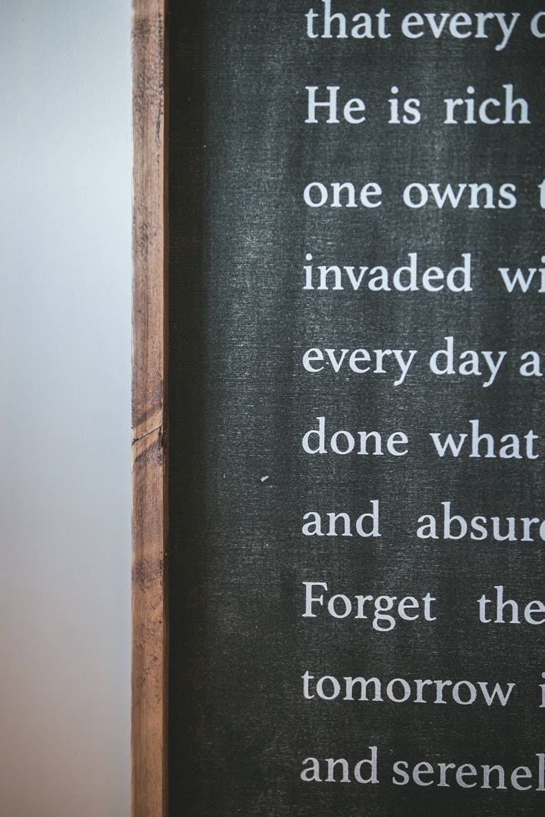 May include: Black chalkboard sign with white text that reads "that every c He is rich one owns t invaded wi every day a done what and absur Forget the tomorrow i and serenel"