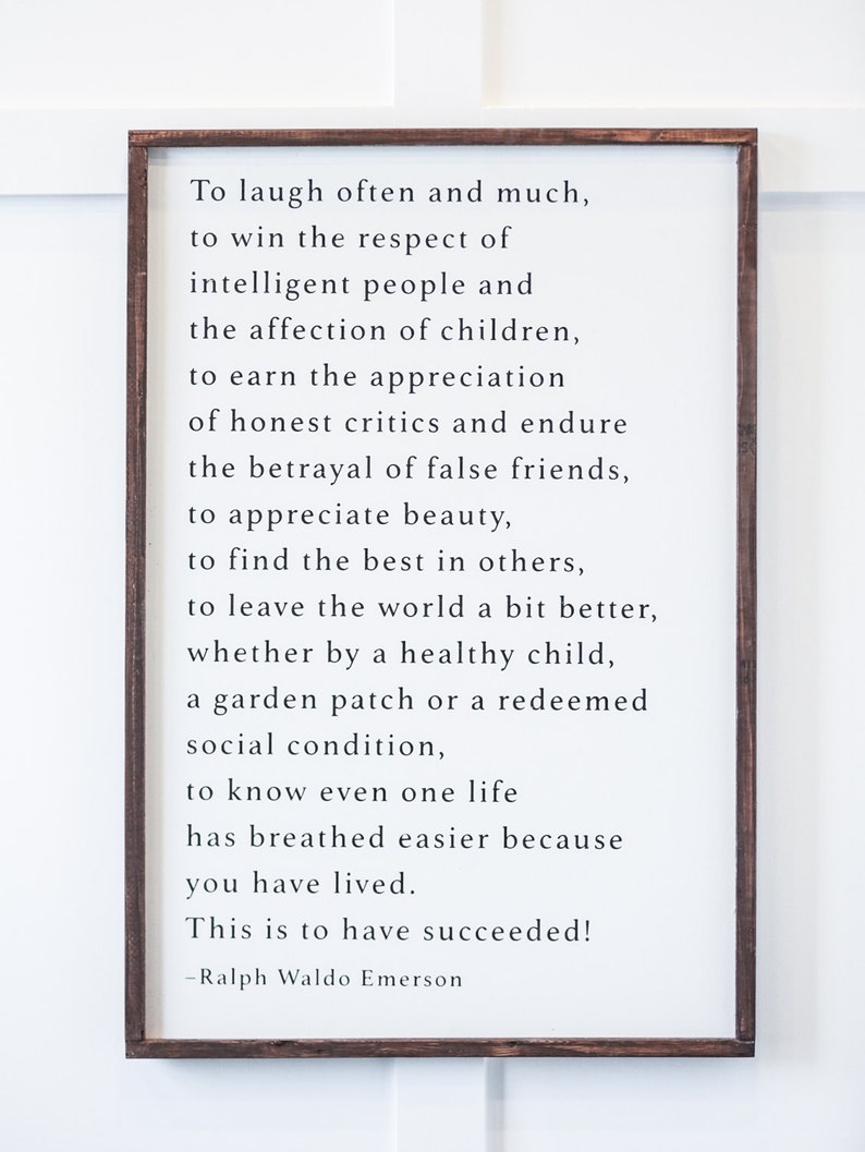 May include: A framed white sign with black text quoting Ralph Waldo Emerson: "To laugh often and much... This is to have succeeded!" The frame is a dark brown color. The sign is a decorative piece.
