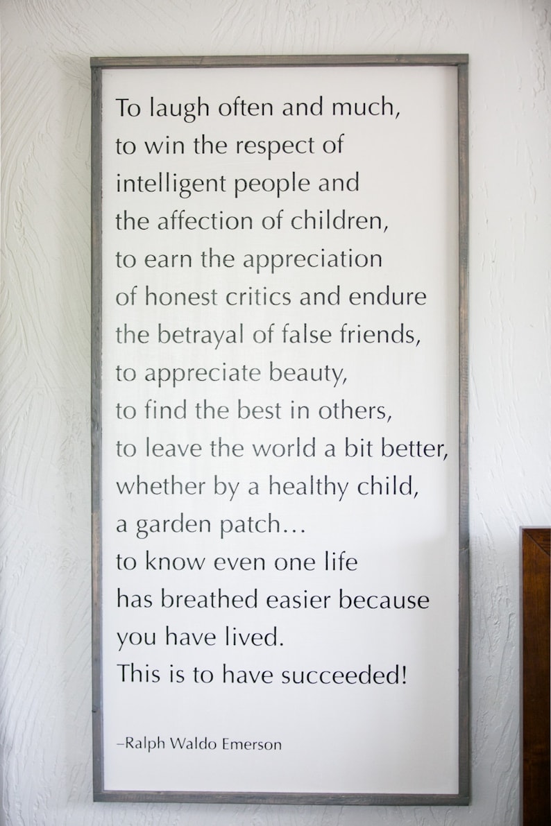 May include: A framed white sign with a gray border displays a quote by Ralph Waldo Emerson. The black text reads, "To laugh often and much... This is to have succeeded!"