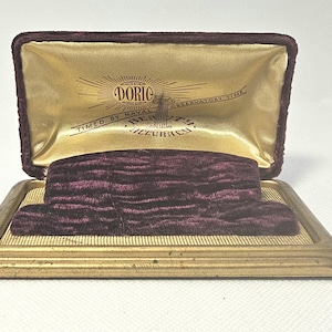 May include: Open vintage watch box with a gold-colored frame and a burgundy velvet interior. The inside lid has gold satin with the text "DORIC" and "TIMED BY NAVAL OBSERVATORY TIME". The box is open, revealing the velvet watch holder.