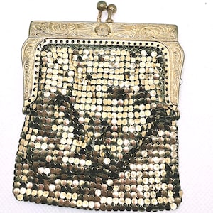 May include: A gold-toned metal mesh coin purse featuring a rectangular frame with an intricate floral engraving and a dual-ball clasp closure. The body of the purse is constructed from small, interlocking metallic discs that create a flexible, shimmering surface texture.