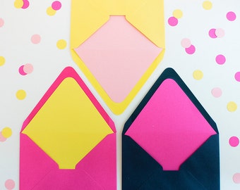 May include: Three colorful envelopes with open flaps, showcasing vibrant interior colors. The envelopes are yellow, pink, and navy blue, with pink, yellow, and pink interiors, respectively. Scattered confetti in pink and yellow dots adds a playful touch.
