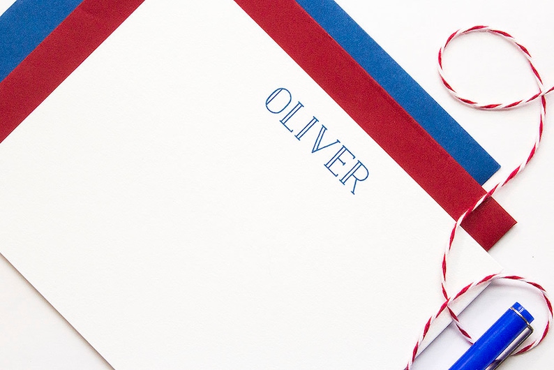 May include: White stationery with the name "OLIVER" printed in blue. Red and blue paper accents are visible, along with a red and white twine and a blue pen. The stationery is likely for personal or professional use.