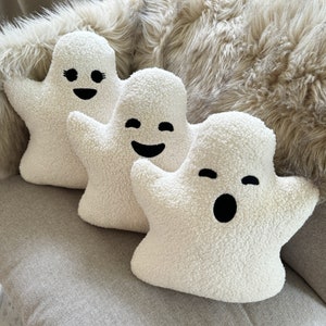 May include: Three white plush ghost-shaped pillows with different facial expressions. The ghosts have black eyes and mouths.