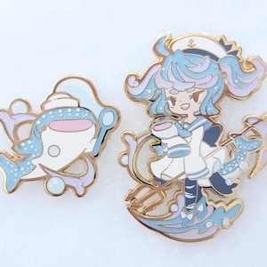Puede incluir: Dos pines esmaltados con diseños náuticos. Uno representa una ballena con gorro de marinero, y el otro muestra a una marinera sosteniendo una taza. Ambos pines tienen contornos dorados y son en tonos azules, blancos y rosas.