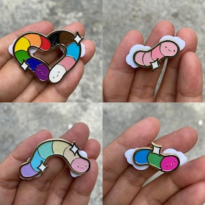 Puede incluir: Una colección de cuatro pines de esmalte con gusanos de dibujos animados con caras sonrientes. Un pin tiene forma de corazón con colores de arcoíris, mientras que los otros son gusanos individuales en combinaciones de rosa, pastel y azul.