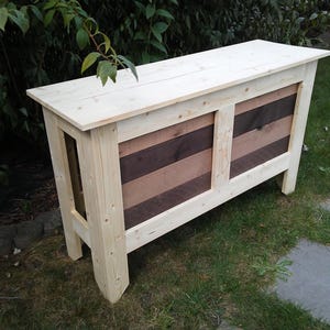 May include: A rectangular wooden console table featuring a light-colored natural pine frame and a contrasting front panel with alternating horizontal slats of light pine and dark stained wood, supported by four sturdy vertical corner legs.