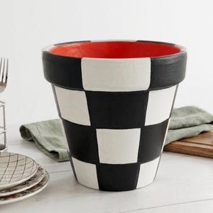 May include: A large, decorative flower pot with a black and white checkerboard pattern. The rim is black, and the interior is painted red. The pot is sitting on a white surface.