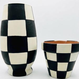 May include: Two ceramic decorative pieces: a tall vase and a small flower pot. Both are painted with a black and cream checkerboard pattern. The vase has a rounded shape, while the pot has a classic flared design.