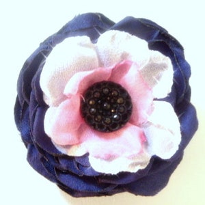 May include: A navy blue fabric flower with a pink and white fabric center. The center has a black rhinestone embellishment.