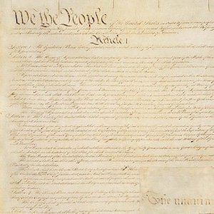 May include: A historical document on aged, off-white parchment paper featuring dark brown cursive calligraphy. The text begins with the prominent heading We the People and continues with Article 1, displaying dense, handwritten legal script throughout.