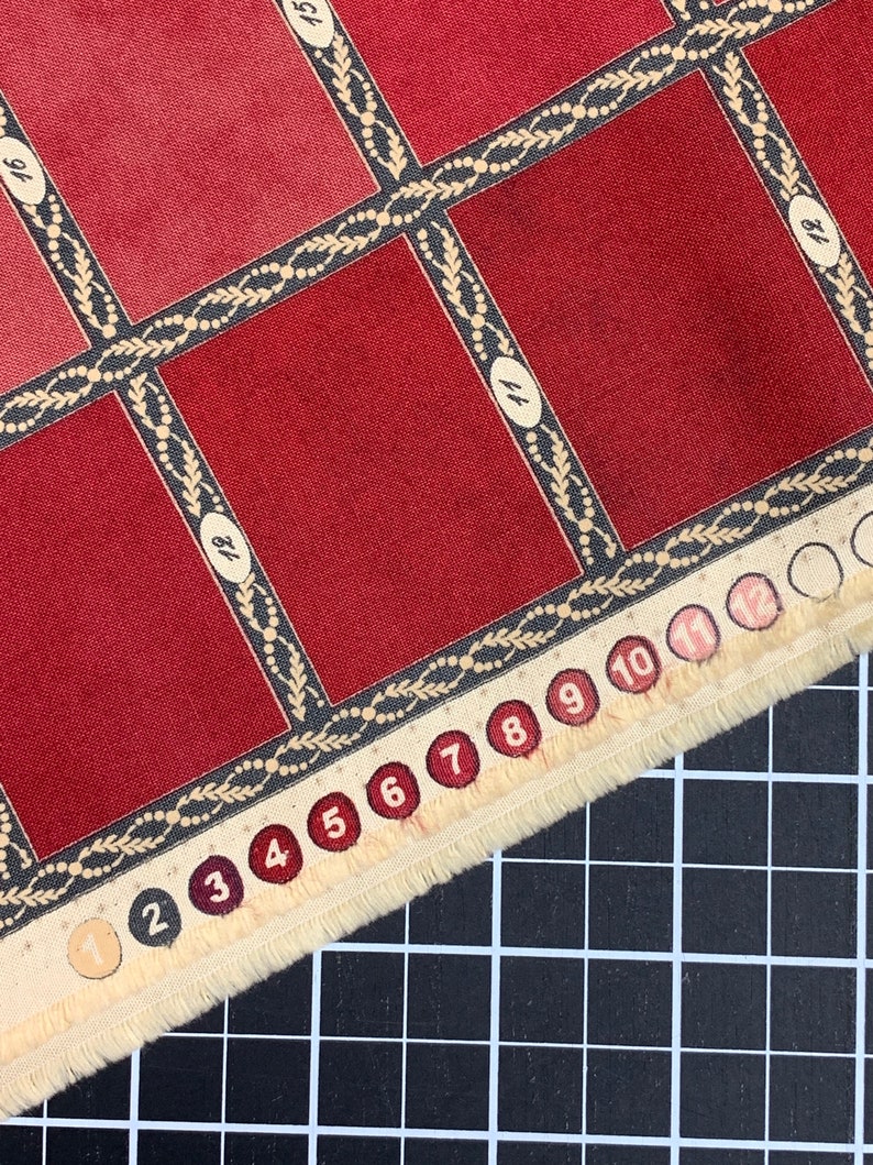 Puede incluir: Una muestra de tela roja con un patr&oacute;n de cuadr&iacute;cula y los n&uacute;meros del 1 al 12 impresos en el borde. La tela tiene un borde decorativo con un dise&ntilde;o de hojas y cuentas.