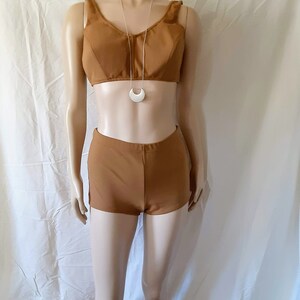 May include: A brown swimsuit with a halter top and high-waisted shorts. The swimsuit is on a mannequin and has a silver crescent moon necklace.