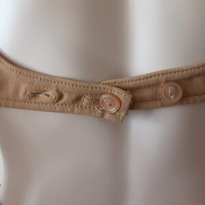 May include: A close-up of the back of a brown garment with two plastic buttons. The buttons are sewn onto a brown fabric strap.