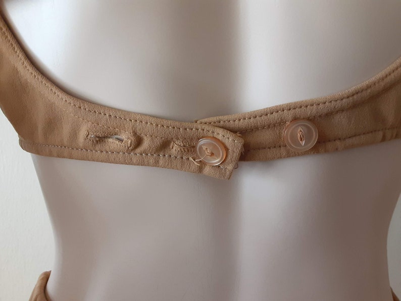 May include: A close-up of the back of a brown garment with two plastic buttons. The buttons are sewn onto a brown fabric strap.