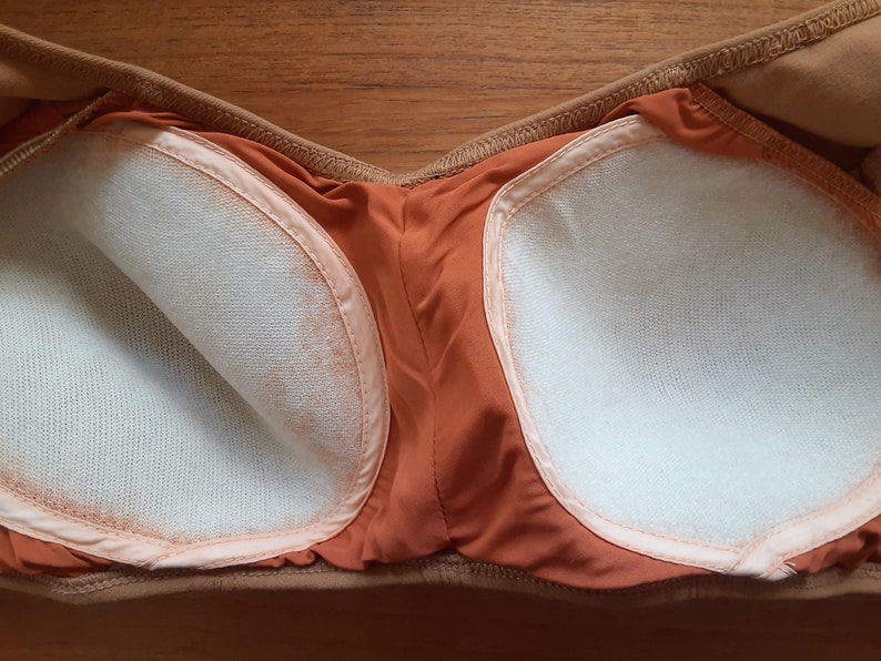 May include: The inside of a strapless bra with brown fabric and white padding.