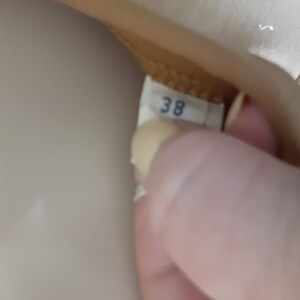 May include: Close-up of a beige leather shoe with a white label that says "38" on it.