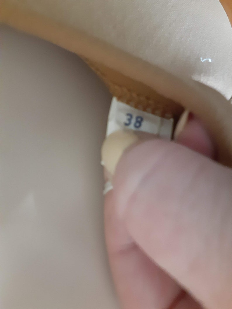 May include: Close-up of a beige leather shoe with a white label that says "38" on it.