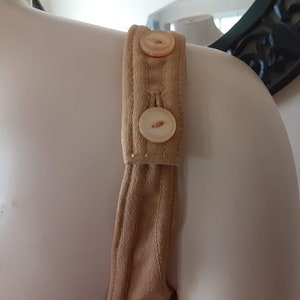 May include: A close-up of the strap of a brown jumpsuit with two white buttons.