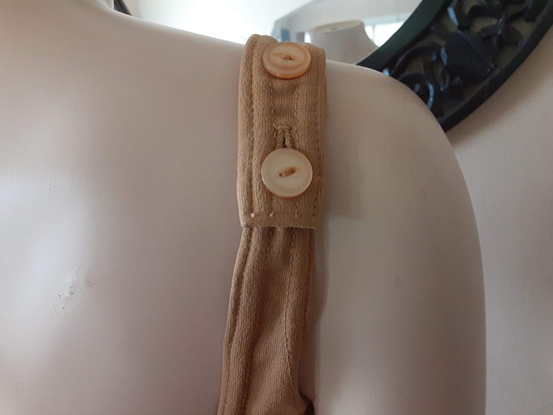 May include: A close-up of the strap of a brown jumpsuit with two white buttons.