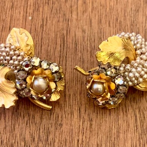 May include: A pair of gold tone earrings with a cluster of faux pearls and rhinestones in a leaf design.
