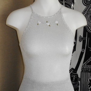 May include: A silver halter top with a shimmering, ribbed texture. The neckline is adorned with small white flowers and green accents. The top is displayed on a white mannequin.