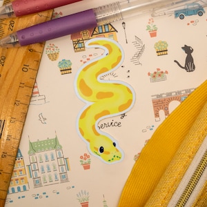 May include: A yellow and white snake sticker with the word "Service" printed below it. The sticker is on a light pink background with a pattern of houses, flowers, and other designs.