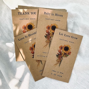 May include: A collection of kraft paper seed packets with sunflower illustrations. The packets have text that reads "Thank You", "Baby in Bloom", "Love is Blooming", and "Let Love Grow". The last packet is personalized with a date.
