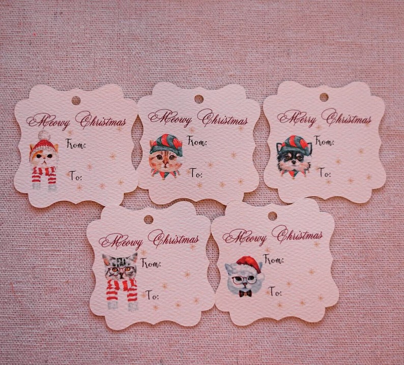 May include: Five decorative gift tags with a scalloped edge. Each tag features a watercolor illustration of a cat or dog wearing a holiday hat and scarf. The text "Meowy Christmas" and "Merry Christmas" are printed on the tags, with space to write "From:" and "To:"