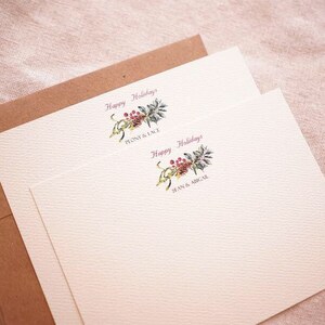 May include: Two white cards with a brown envelope. The cards have a floral design with red berries and green leaves. The text on the cards reads "Happy Holidays".