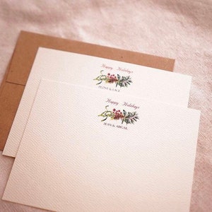 May include: Two white cards with a green and red floral design and the text "Happy Holidays" with the names "Flynn & Lacy" and "Sean & Abigail" printed below.