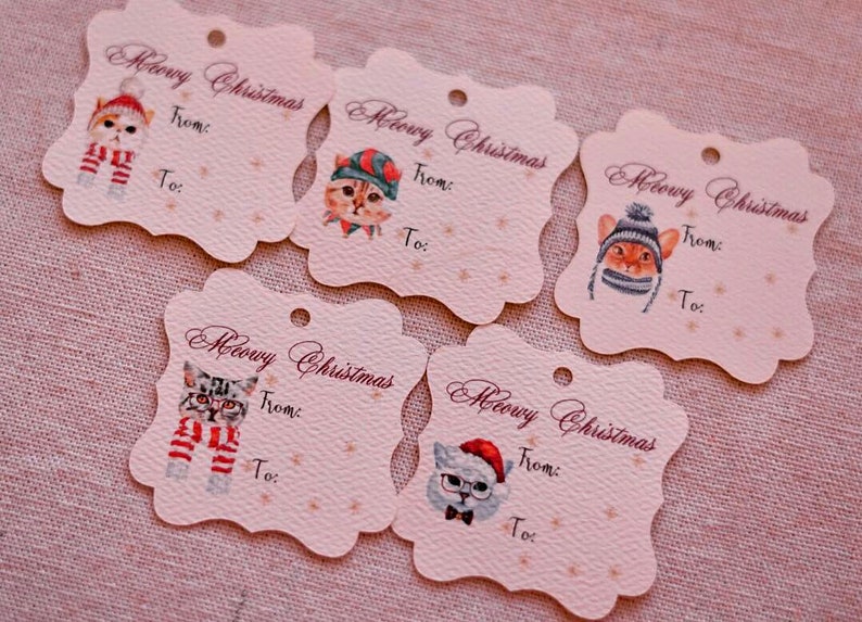 May include: Five decorative gift tags with scalloped edges. Each tag features a watercolor illustration of a cat wearing a winter hat and scarf. The tags read "Meowy Christmas" with space for "From:" and "To:"