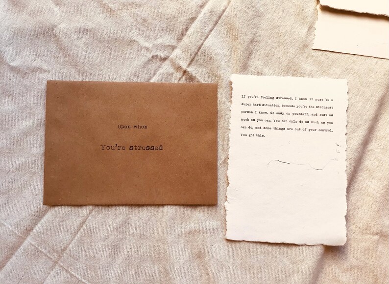 May include: A brown paper envelope with the words "Open when you're stressed" printed on the front. The envelope contains a handwritten note that reads: "If you're feeling stressed, I know it must be a super hard situation, because you're the strongest person I know. Go easy on yourself, and just do as much as you can. You can only do as much as you can do, and some things are out of your control. You got this."