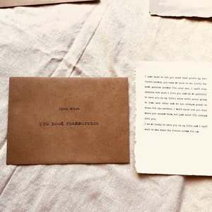 May include: A brown envelope with the words "Open when you need reassurance" printed on it. Next to the envelope is a handwritten note that reads: "I just want to let you know that you're my favorite person. You mean so much to me. You're the most genuine person I've ever met. I can't explain how much I love you and I am grateful to have you in my life! We are never going to lose each other and we know we'll always be there for another. I don't know how you feel about me spending this, but just know I'll always love you. I am so lucky to have you in my life, and I can't wait to see what the future holds for us."