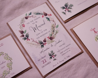 Könnte beinhalten: Ein Satz Hochzeitseinladungen mit Winterthema. Die Einladungen zeigen eine Aquarell-Illustration eines Kranzes mit Stechpalme, Tannenzapfen und Grün. Der Text auf den Einladungen lautet "Es ist die Zeit zum Heiraten" und enthält die Namen des Paares, das Hochzeitsdatum, die Uhrzeit und den Ort. Die Einladung enthält auch eine kleinere Karte mit dem Datum der Hochzeit.