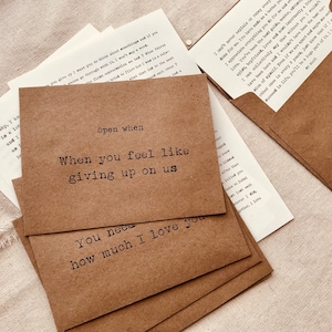 May include: A set of brown paper envelopes with white text on each. The text reads "Open when" followed by a phrase. The phrases are "When you feel like giving up on us" and "You need how much I love you".