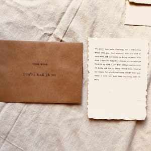 May include: A brown envelope with the text "Open when you're mad at me" on the front. A handwritten note on a piece of paper reads "I'm sorry that we're fighting, but I absolutely will love you. Take whatever time you need to calm down, and I probably am doing the same. Even when I make the biggest mistakes, you are always first in my mind. I just don't always realize what I'm doing and how it makes others feel. This is our chance for growth and being honest with each other. I love you more than anything, and I'm sorry."