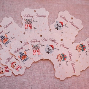 May include: A collection of cream-colored gift tags with a scalloped edge. Each tag features a watercolor illustration of a cat wearing a hat, scarf, or glasses, with the words "Meowy Christmas" and space for "From:" and "To:"
