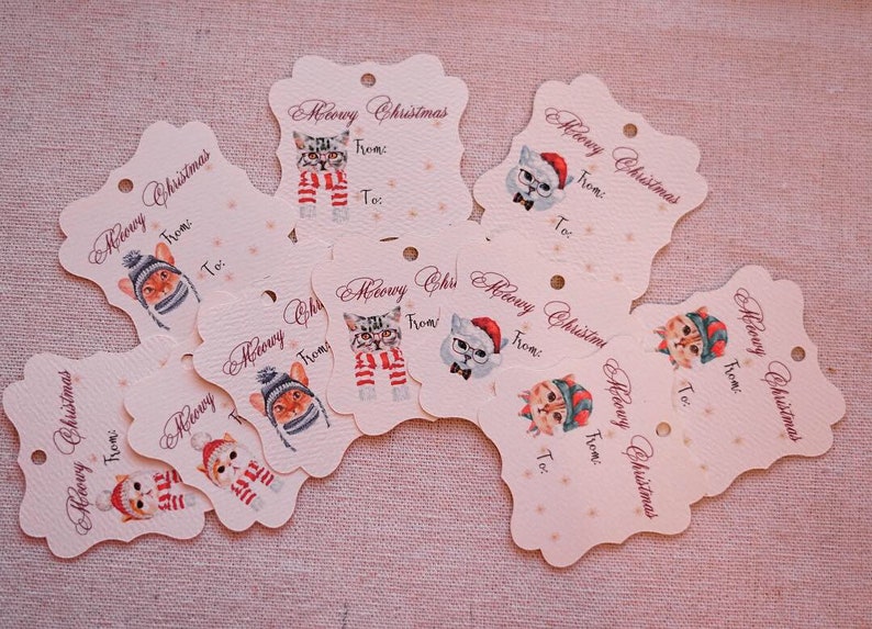 May include: A collection of cream-colored gift tags with a scalloped edge. Each tag features a watercolor illustration of a cat wearing a hat, scarf, or glasses, with the words "Meowy Christmas" and space for "From:" and "To:"