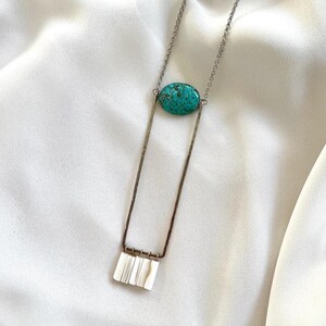 May include: A silver chain necklace with a turquoise oval pendant and a silver bar with a row of white shell pieces hanging from it.