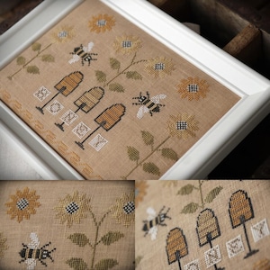 May include: Cross-stitch picture in a white frame. The design shows bees, sunflowers, and beehives on a tan background. The word "HONEY" is stitched below the beehives. The artwork is detailed with yellow, white, and green thread.