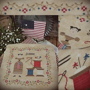 May include: Cross-stitch sampler with an American flag, floral border, and patriotic imagery. The design includes a woman in a dress with an American flag, scissors, spools of thread, and floral accents in red, white, and blue.