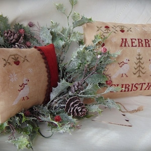 Op de afbeelding: Twee geborduurde kussenslopen met een kerstthema. De grotere kussensloop heeft de tekst "Merry Christmas" met twee vogels en een dennenboom. De kleinere kussensloop heeft een enkele vogel en een hulsttak.