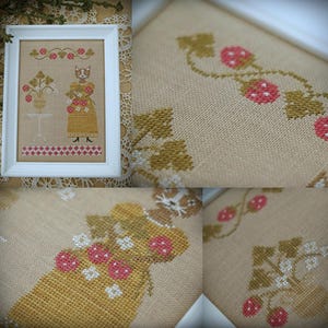 May include: A cross-stitch pattern featuring a cat holding a basket of strawberries. The cat is wearing a yellow dress with white flowers and is standing on a red and white checkered floor. The background is a beige linen fabric with a vine of green leaves and red strawberries.